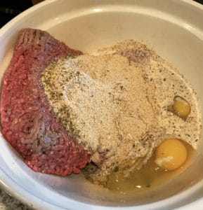 mixing ground beef with bread mixture and eggs to make sunday sauce with meatballs