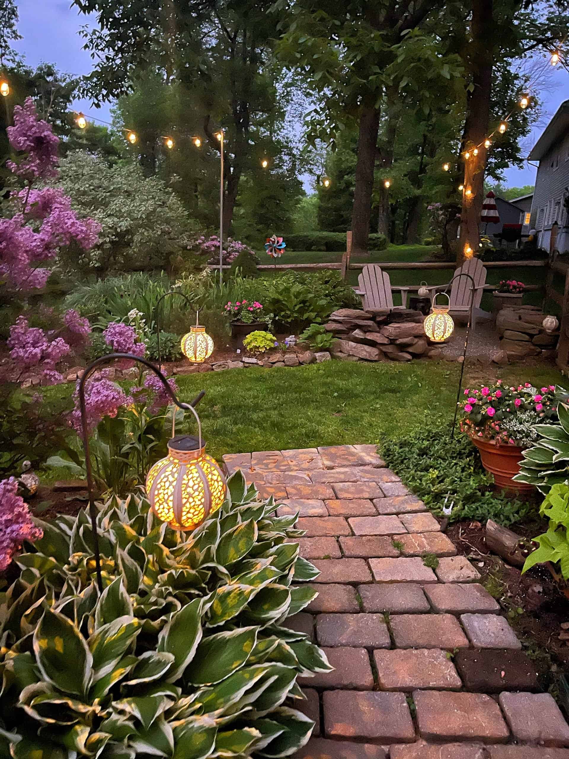 Lilac flowers by the Fire Pit Garden at night lit with solar lanters and surrounded by hostas and twinkle lights