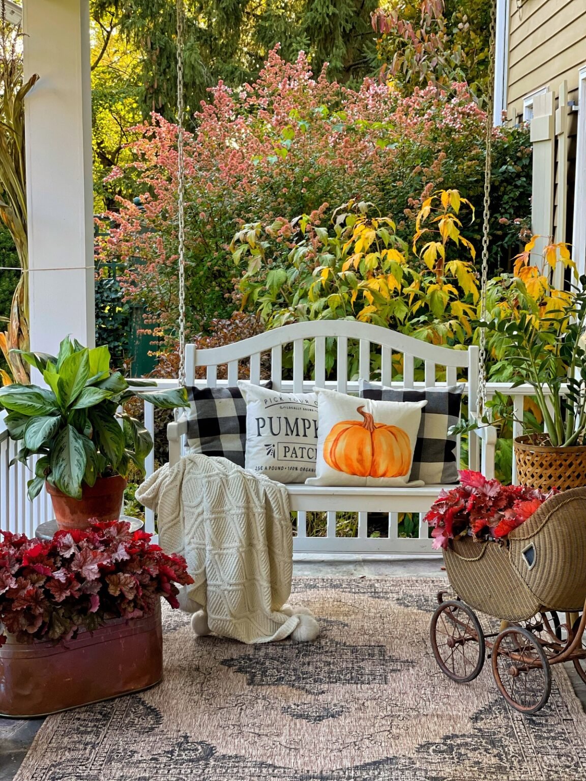 Front porch swing in fall with heuchera, chinese evergreen, zzz plant, fall throw pillows and area rug in fall