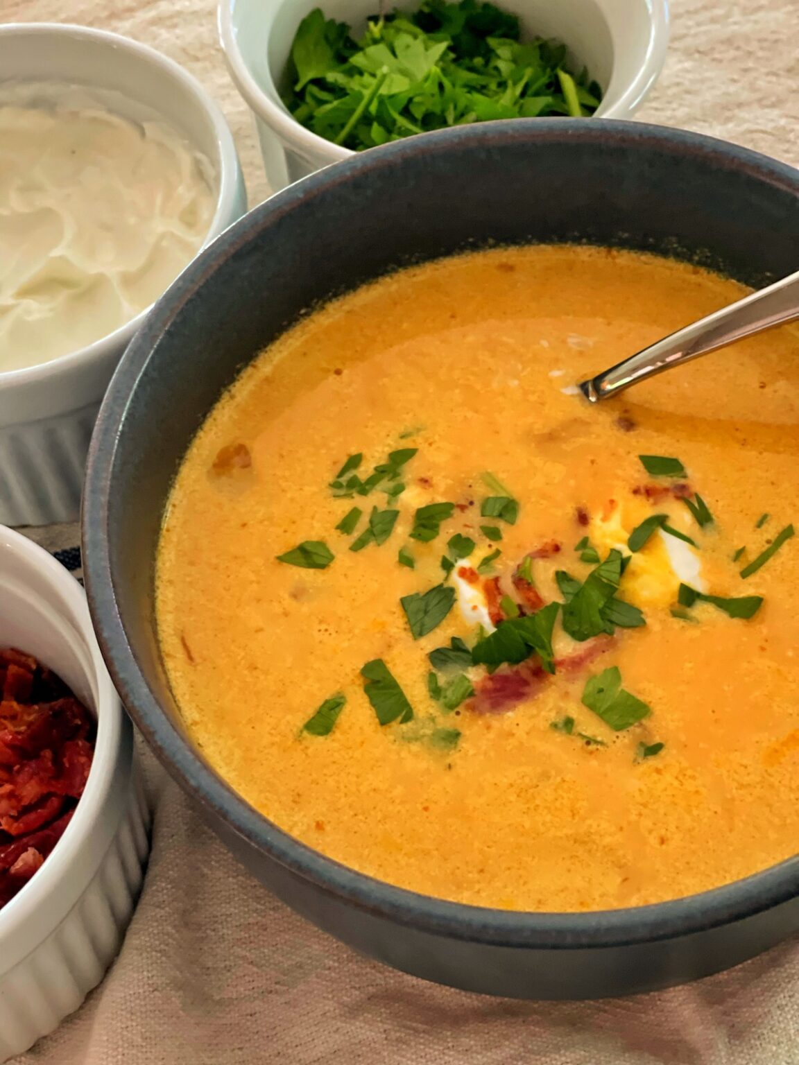close up of pumpkin soup in blue Hearth and Hand Bowl with toppings of bacon, sour cream, and chopped parsley