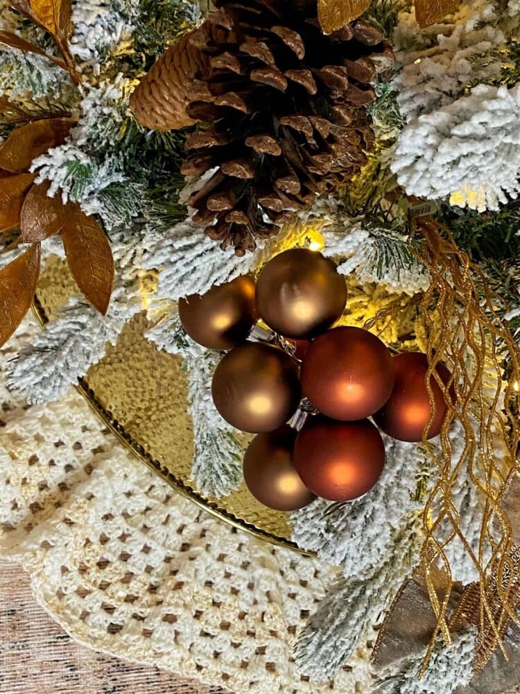 close up of neutral organic textured ornaments on flocked christmas tree with hammered gold tree collar and crocheted christmas tree skirt