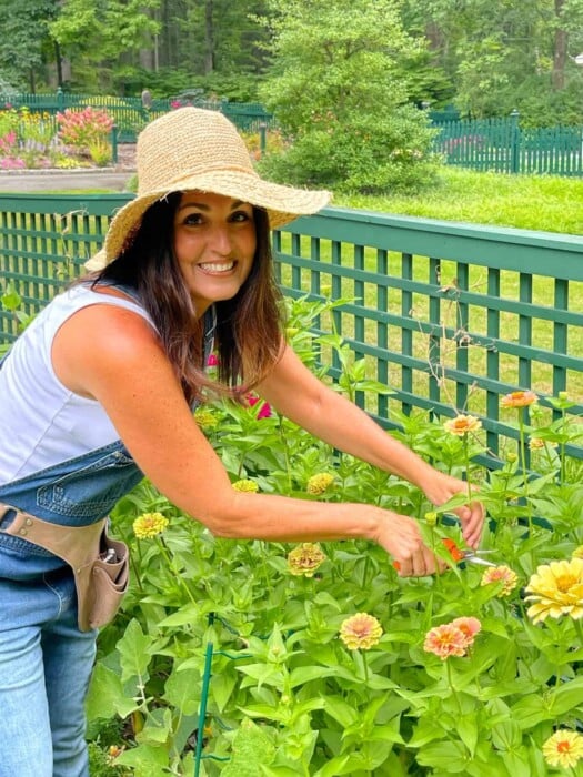 A smiling gardener, Stacy Ling, in a straw hat lovingly tending to a vibrant garden of zinnias, showcasing the joy of horticulture