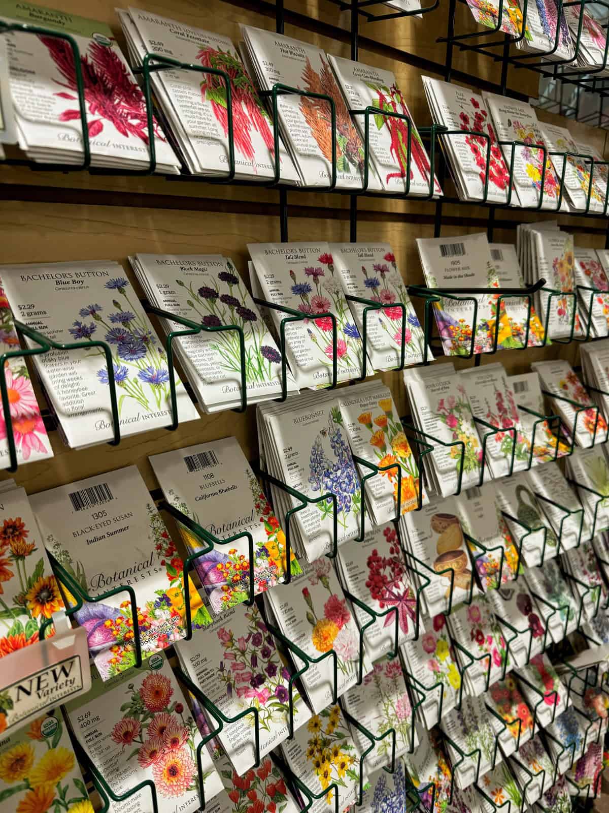 A display of various flower seed packets arranged on racks, showcasing colorful illustrations of different flowers, including daisies, poppies, and cornflowers.
