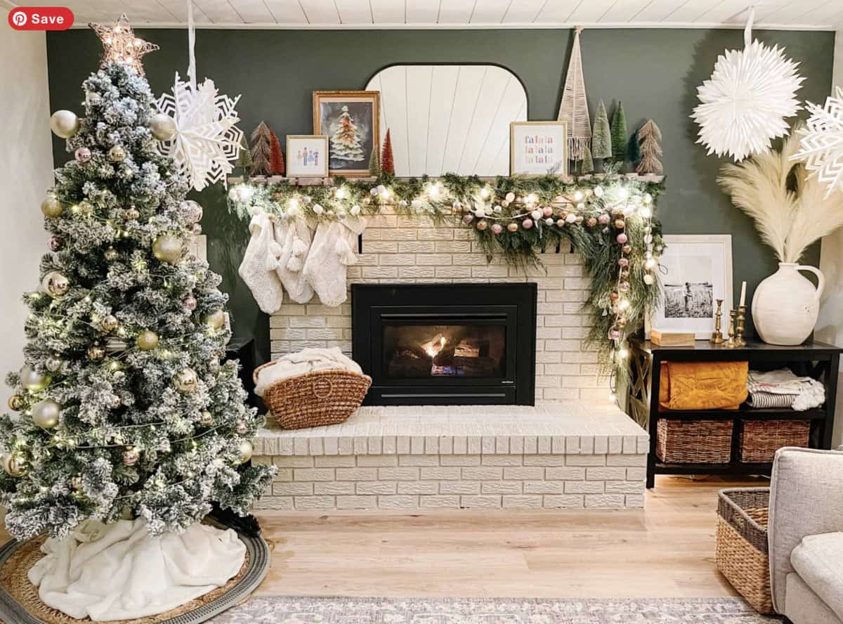 A cozy living room with a decorated Christmas tree, a white brick fireplace adorned with stockings, garland, and string lights, woven baskets, framed art, and neutral holiday decor.