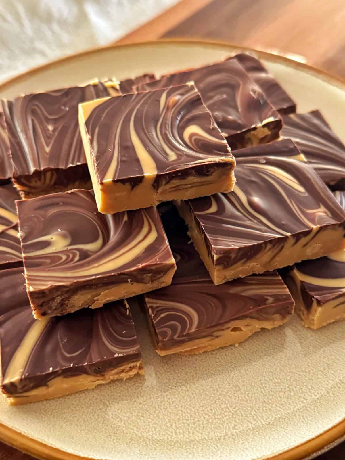 A plate stacked with square pieces of fudge featuring a marbled swirl pattern of dark and light brown, likely chocolate and peanut butter.
