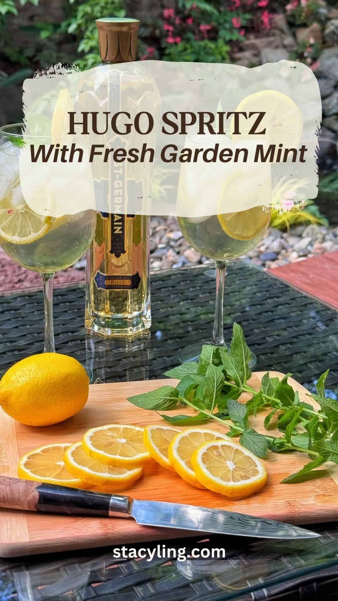 Two glasses of Hugo Spritz with lemon slices and fresh garden mint sit beside a bottle of liquor, lemons, mint sprigs, and a cutting board with a knife on an outdoor glass table. Text reads: "Hugo Spritz With Fresh Garden Mint.